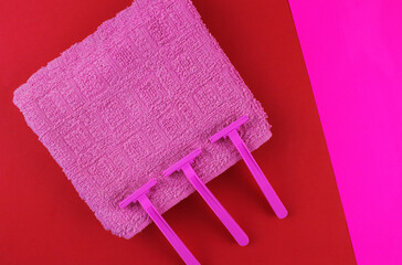 Three shaving razors with pink towel on red and pink background