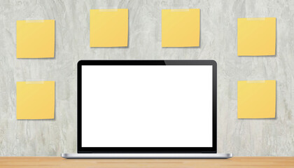 White blank screen laptop on the wood table with yellow blank sticky notes on wall background