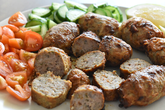 Sheftalia: Cypriot Lamb and Pork Sausages.  Grilled Sausages with Fresh Vegetables (Cucumber and Tomato) on a White Plate. Traditional Cypriot food. 