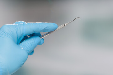 Close up of dentist's hand in blue gloves presenting dental instrument