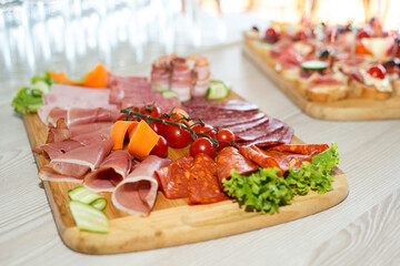 The buffet at the reception. Assortment of canapes on wooden board. Banquet service. Catering, snacks with different types of cheese and meat. Party Concept.