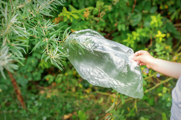 Child's hand removes the plastic bag from a branch in the park