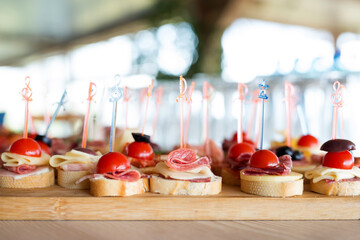 The buffet at the reception. Assortment of canapes on wooden board. Banquet service. Catering, snacks with different types of cheese and meat. Party Concept.