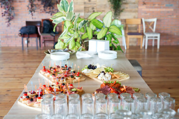 The buffet at the reception. Assortment of canapes on wooden board. Banquet service. Catering, snacks with different types of cheese and meat. Party Concept.