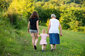 Rear view of a girl holding her grandmother and mother by hand walking.