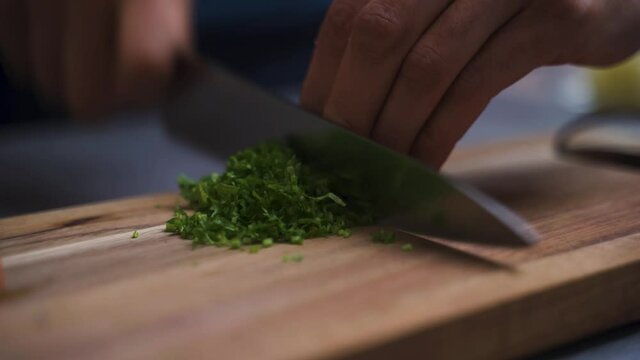 Chef chopping herbs on a wooden board.