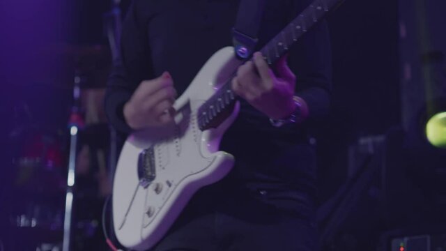 Close-up shot of a man's hand playing an electric guitar on stage. Six-string guitar. The guitarist in black performs on stage, rock music concert. 