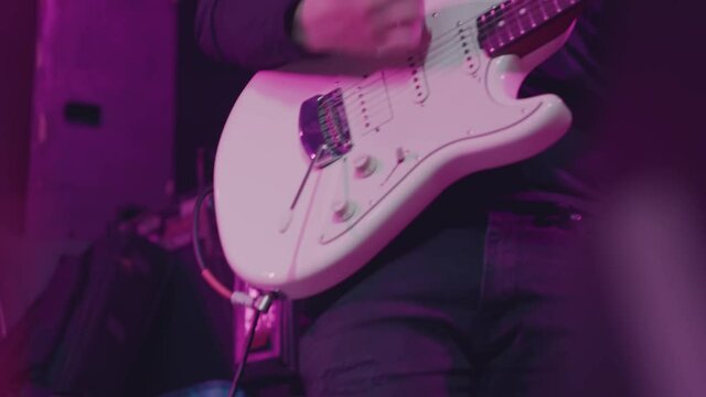 Close-up shot of a man's hand playing an electric guitar on stage. Six-string guitar. The guitarist in black performs on stage, rock music concert. 
