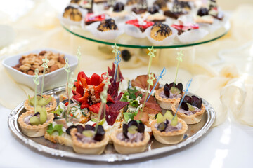 The buffet at the reception. Assortment of canapes on a table. Banquet service. Catering food, snacks with different types of cheese, ham, salami, prosciutto, shrimp, vegetables and fruits. 