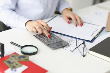 Business woman with red manicure counting on calculator in office closeup