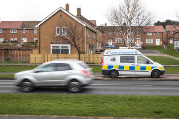 Police Camera Enforcement Unit Van parked at side of the road to enforce speed restrictions.  Speed camera sign visable as blurred silver car passes
