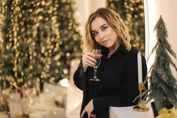 Beautiful blond hair woman in black shirt with glass of champagne selebrate new year in front of Christmas tree