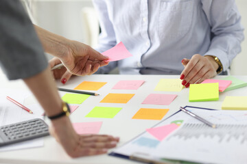 Woman giving pink sticker to colleague at table at workplace in office