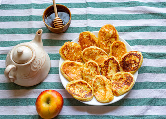 Flat lay composition with tasty homemade pancakes laid out on plate near an apple, teapot and bowl...