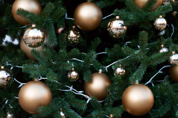 Closeup view of green christmas tree decorated with golden balls and lights.