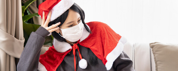 Obraz premium Unhappy Xmas woman in Santa clause suit having headache wearing face mask due to coronavirus and COVID-19 outbreak in Christmas period, concept of Covid Christmas or new normal social distancing Xmas