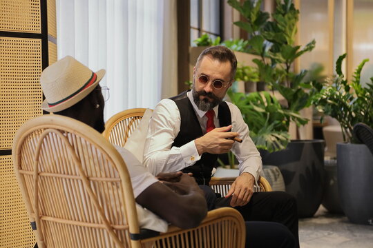 Caucasian Businessman In Formal Wear And His African American Friend In Luxury Tropical Style Hotel Lobby