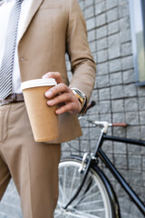 cropped view of businessman in suit holding coffee to go near building