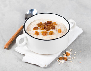 Multi grain milk porridge with raisins in a bowl on a light gray background
