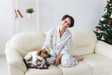 Happy young woman wearing pajama in living room with christmas tree. Holidays concept.