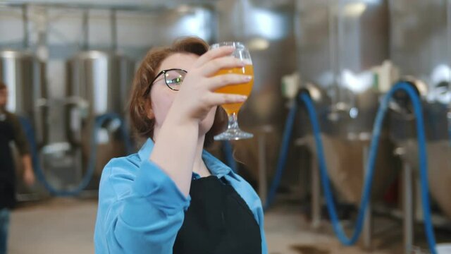 Portrait of woman brewer holding glass with craft beer and drinking