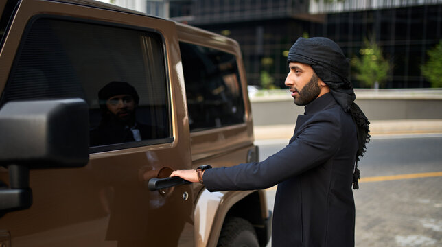 Arab man opening door of luxury vehicle wearing traditional suite with keffiyeh