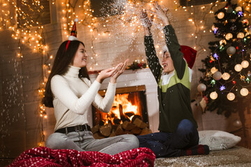 Children under Christmas tree at home celebrate winter holidays, they are having fun with fake snow.