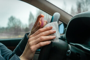 Female driver's hands wipe the steering wheel of the car with antiseptic and wipes close-up