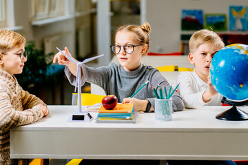 Renewable energy, kids, technology, science and people concept . Group of thoughtful kids study about ecology problems and their solution with wind turbine model and globe at school.