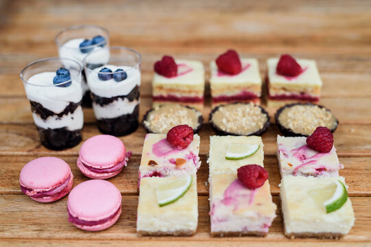 Selection of colorful and delicious cake desserts on rusty wooden table.
