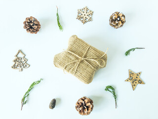 Arrangement of wooden christmas ornaments, pine cones and pine branches with a christmas present box in the middle on an isolated white surface, top view
