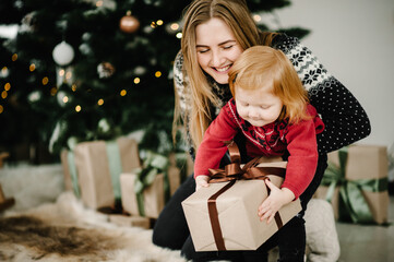 Obraz na płótnie Canvas Child surprising his mother with a Christmas gift. Family open present gift box. Merry Christmas and Happy Holidays. Happy New Year 2021.