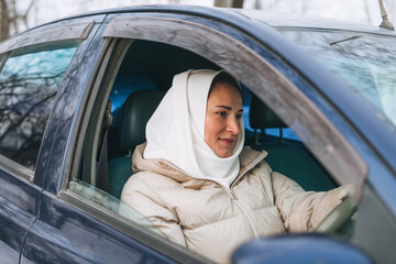 Beautiful smiling young Muslim woman in headscarf in light clothing in the right-hand-drive car