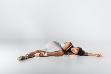 graceful african american ballerina in dress lying on floor on white background