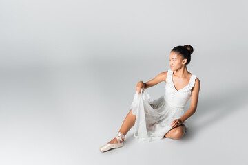 graceful african american ballerina in dress dancing on floor on white background
