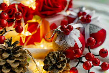 Christmas decorations on a soft cozy white blanket. Red toys in the form of balls and berries, with fir cones. Around yellow lanterns light bulbs in the form of stars. Elegant composition for Christma