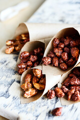 Caramelized sugared peanuts in paper envelope bags on wooden background. Selective focus