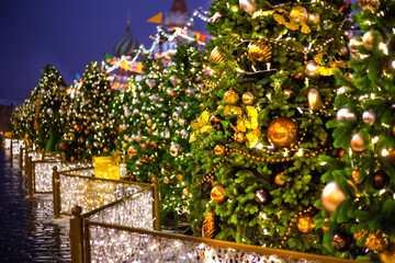 Row of Christmas pine trees with colorful garlands, decorations, balls and toys on street at night. Holiday, celebration, traditional and new year concept