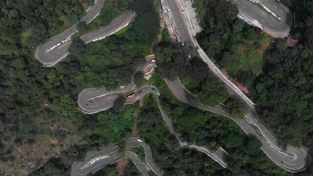 Hairpin bends in Yercaud, India covered with endless vast green forest with trees growing rapidly vehicles passing on the road.