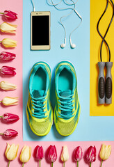 Fototapeta na wymiar Sport shoes, skipping rope, smartphone with earphones and tulips on pastel background, copy space. Overhead shot of running foot wear. New sneakers. Top view, flat lay