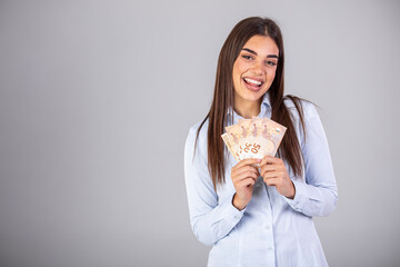 Super excited young woman holding bunch of Euro banknotes, clinching fists, celebrating winning lottery. Ecstatic woman holding lots of money, isolated on gray background.