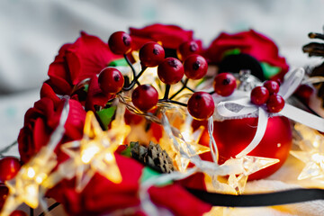 Christmas decorations on a soft cozy white blanket. Red toys in the form of balls and berries, with fir cones. Around yellow lanterns light bulbs in the form of stars. Elegant composition for Christma