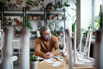 Frustrated owner sitting at table in closed cafe, small business lockdown due to coronavirus.