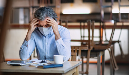 Frustrated owner sitting at table in closed cafe, small business lockdown due to coronavirus.