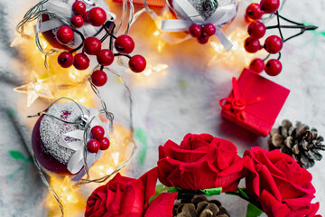 Christmas decorations on a soft cozy white blanket. Red toys in the form of balls and berries, with fir cones. Around yellow lanterns light bulbs in the form of stars. Elegant composition for Christma