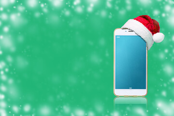 Smartphone in Santa Claus hat, on a green background. Copy space.