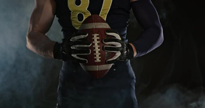 American football sportsman player holding a ball on black background close up