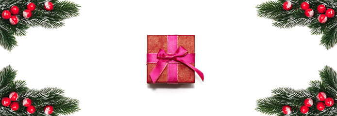 Red gift box is surrounded with decorative Christmas snowy frosted fir twigs with red berries. Copy space in the middle. Christmas card, winter holidays concept. Isolated on white background. Banner