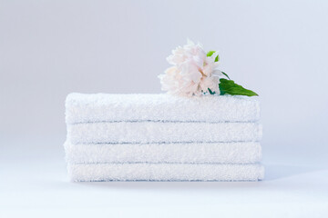 Four white neatly folded terry towels with a delicately pink peony flower on a light background.