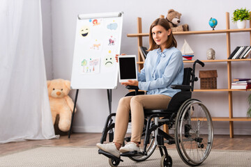 Full length of female psychologist showing digital tablet while sitting in wheelchair in office